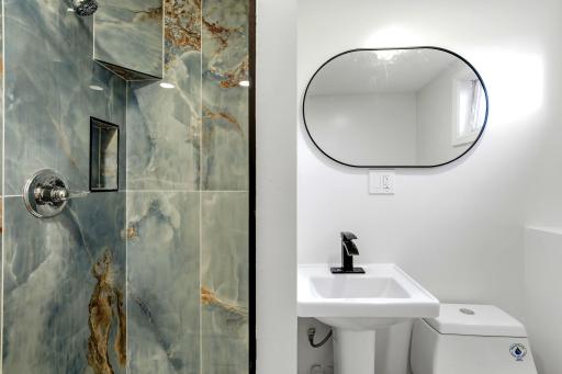 Strikingly renovated three-quarter bathroom featuring a walk-in shower with dramatic marble-look tile, built-in niches, a modern pedestal sink, and sleek black accents. The bold finishes create a stylish, spa-inspired space that truly stands out.