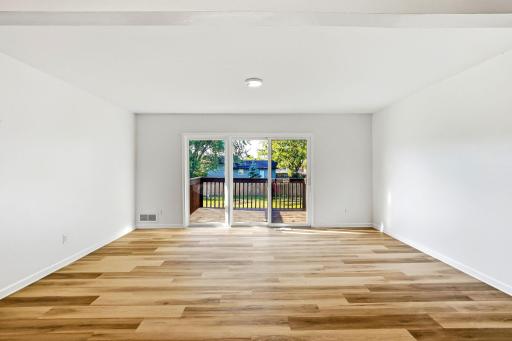 Bright and spacious living room featuring new flooring, fresh paint, and large sliding glass doors that fill the space with natural light and provide direct access to the backyard deck.