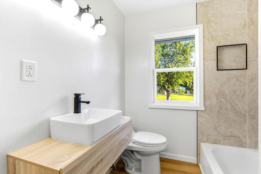 Beautifully renovated main-floor bathroom featuring a modern floating vanity, stylish vessel sink, contemporary black fixtures, and a tiled tub-and-shower surround.
