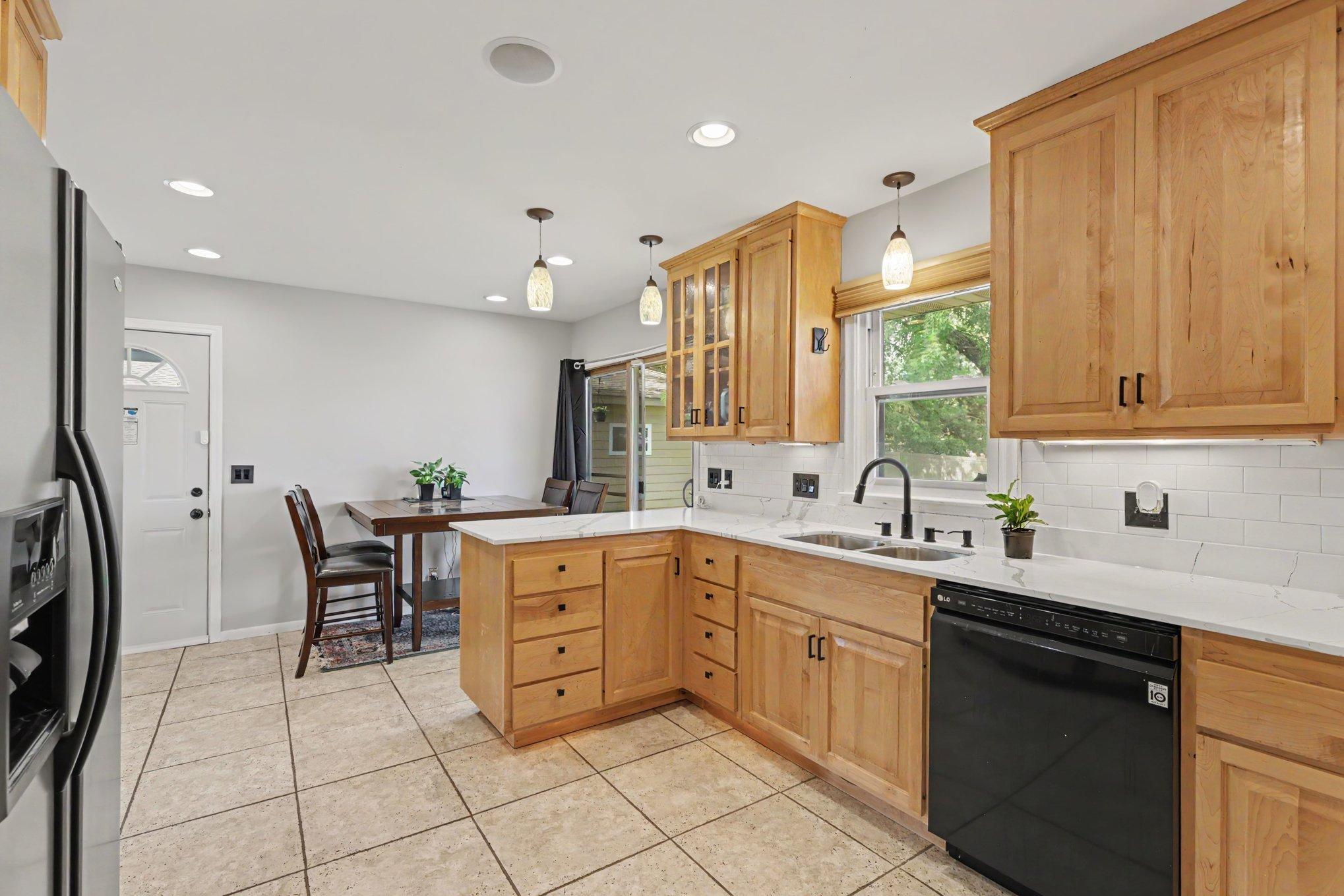 The kitchen and informal dining area are lit with recessed lights, decorative pendant lights, and natural light from the kitchen window and the patio door to the backyard.