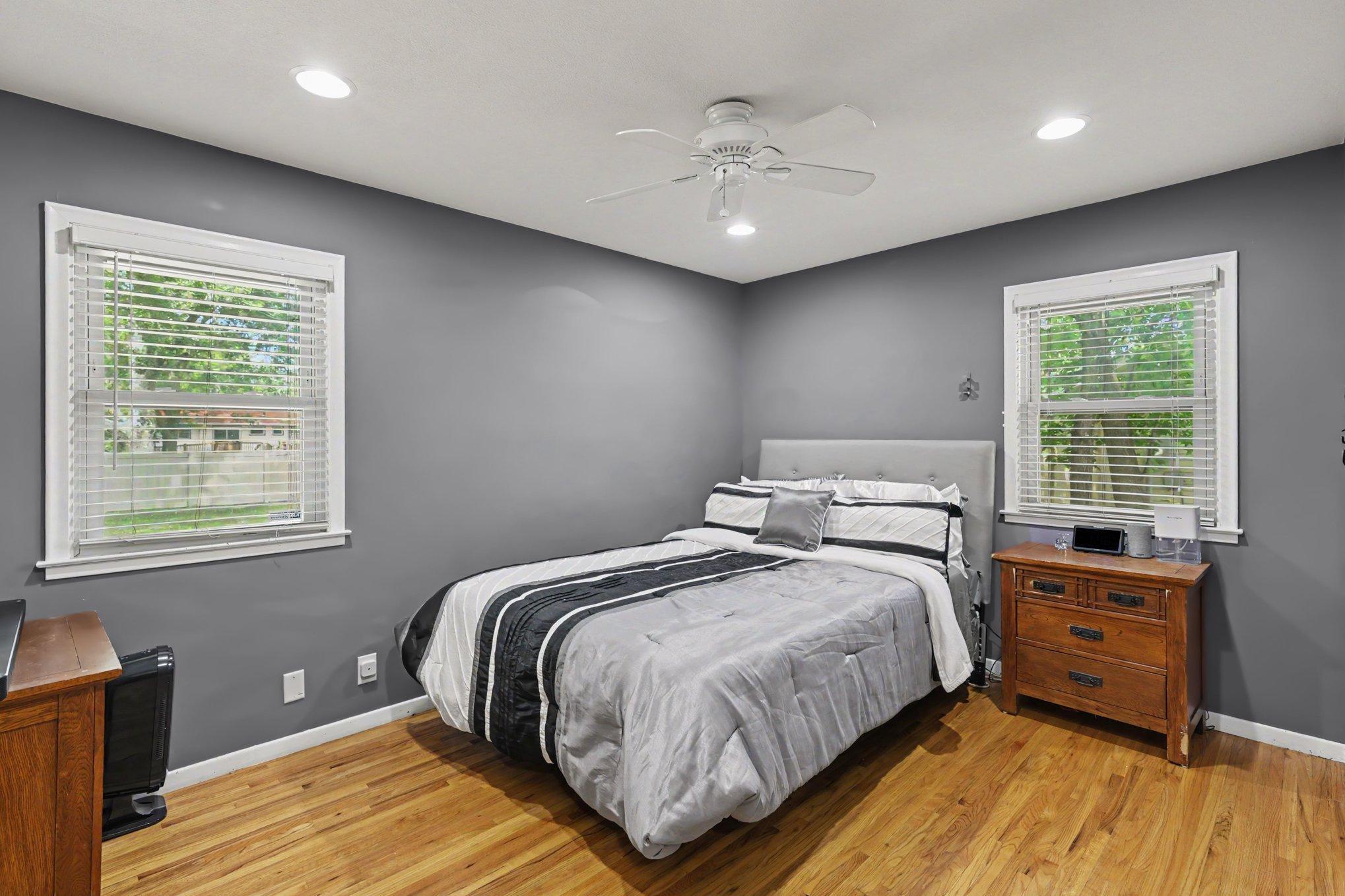 The primary bedroom features hardwood floors, two windows, recessed lights, and a ceiling fan.