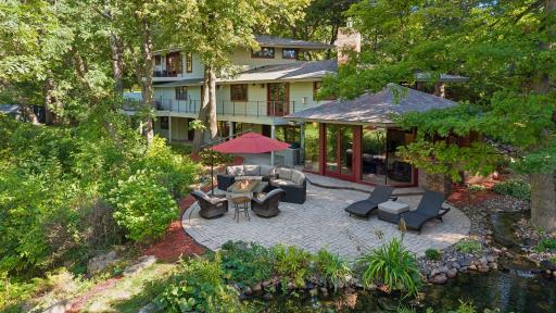 A distinctive waterfall-style water feature flows into a tranquil pond beside the home, creating a peaceful focal point within the mature, wooded landscape.