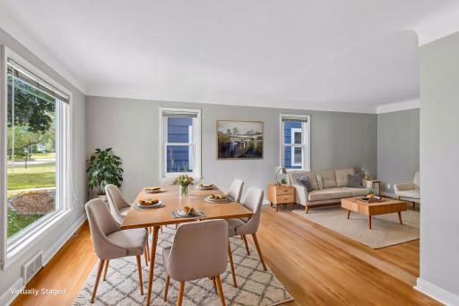 Virtually staged informal dining room and living room with original hardwood floors, fresh paint, coved ceilings and a large picture window flooding the rooms with morning light.