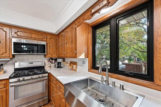 Filled with natural light, the updated kitchen showcases an Anderson window, farmhouse stainless steel sink, tile backsplash, and hard-surface countertops, blending style and functionality.