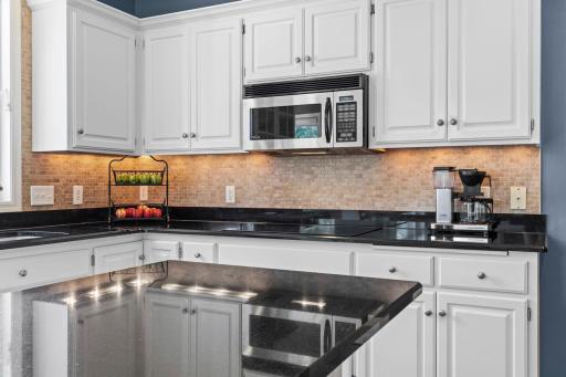 Travertine tile backsplash beautifully complements the crisp white cabinetry and dark granite surfaces.