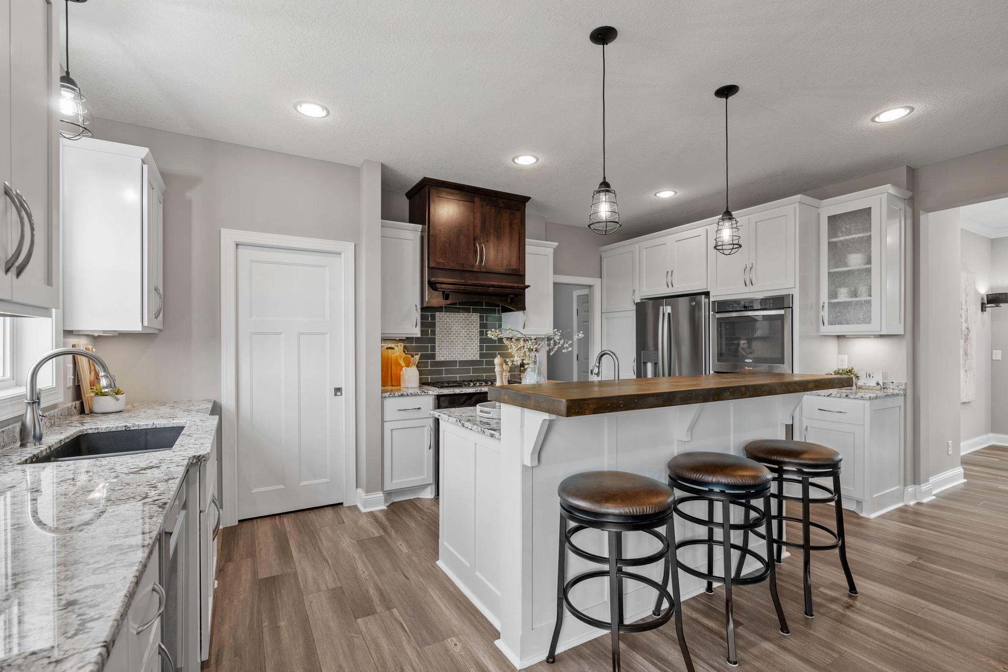 Gourmet Kitchen w/ granite + butcher-block counters, white cabinetry, subway tile backsplash, SS apps incl Thermador gas cooktop + double ovens, hood, beverage fridge + pantry