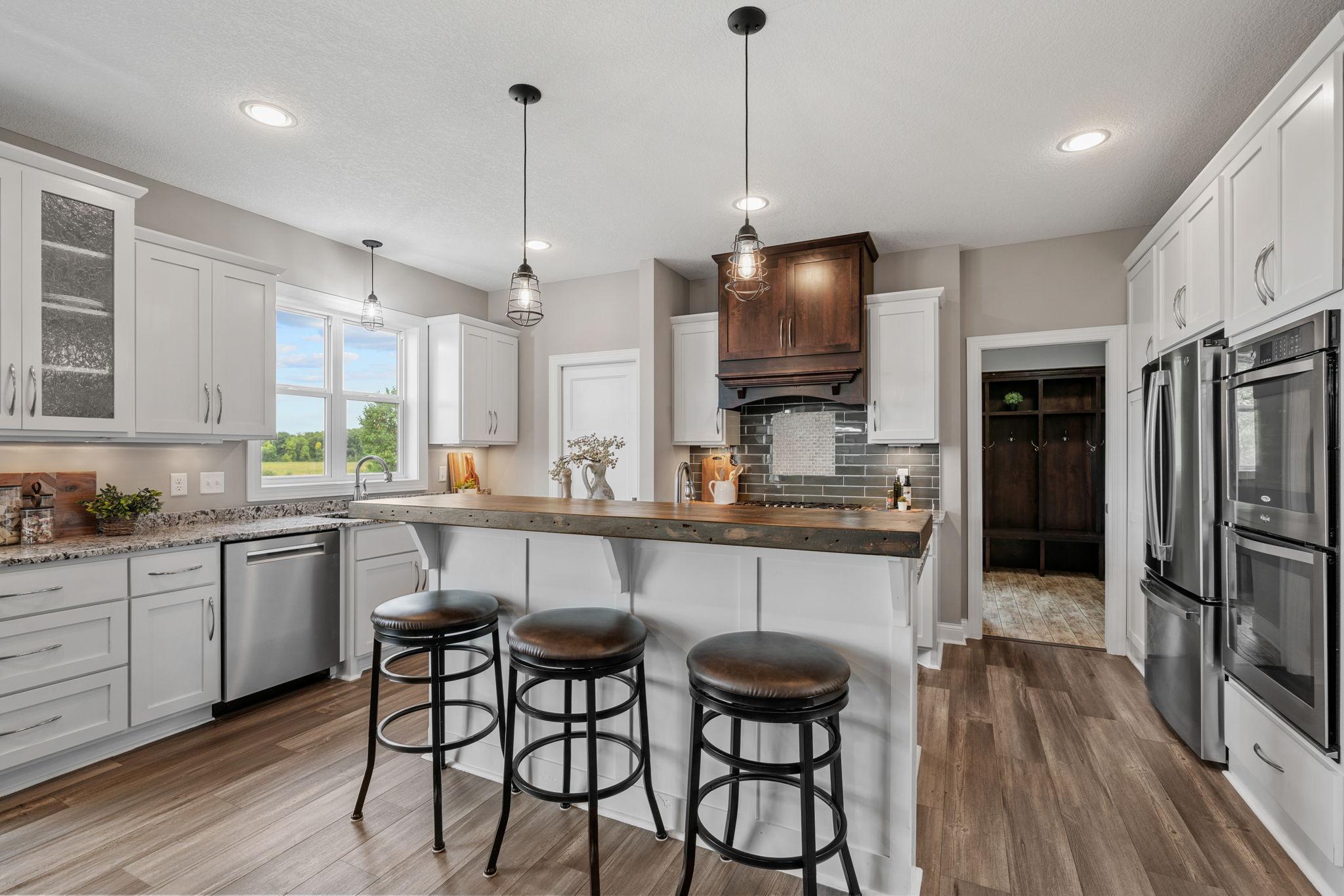 Gourmet Kitchen w/ granite + butcher-block counters, white cabinetry, subway tile backsplash, SS apps incl Thermador gas cooktop + double ovens, hood, beverage fridge + pantry