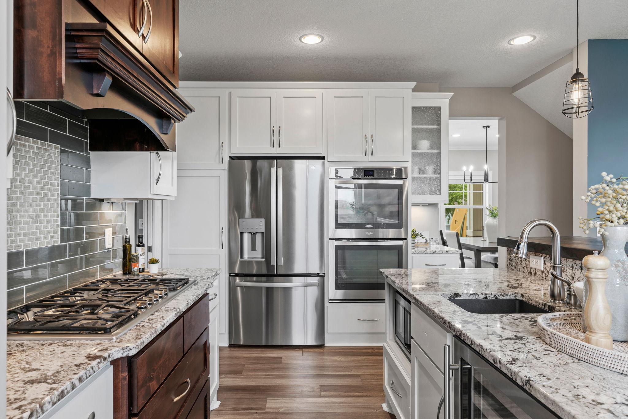 Gourmet Kitchen w/ granite + butcher-block counters, white cabinetry, subway tile backsplash, SS apps incl Thermador gas cooktop + double ovens, hood, beverage fridge + pantry