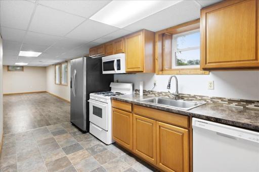 Another view of the lower-level kitchen highlights the cabinetry, appliances, dishwasher, and open connection to the living area