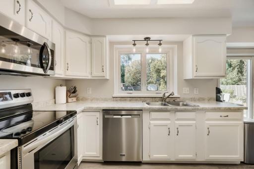 White kitchen with stainless steel appliances, including a new dishwasher. The kitchen window overlooks the big backyard.