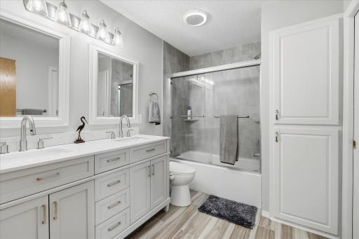 Beautifully newly updated full bathroom features a double-sink vanity, modern finishes, ceramic tile flooring, and a tub/shower with tiled surround and glass doors.