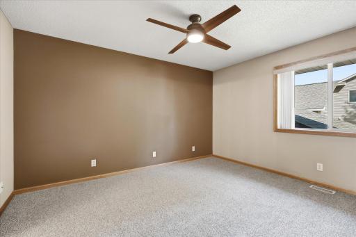 Spacious primary bedroom offers newer carpet, a ceiling fan, neutral décor, and a large window providing plenty of natural light.