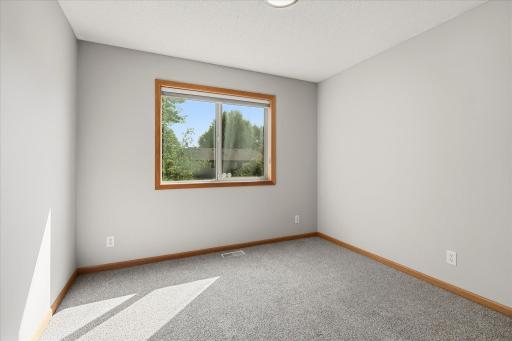 Additional upper-level bedroom offers newer carpet, neutral finishes, and a large window overlooking the mature trees outside.