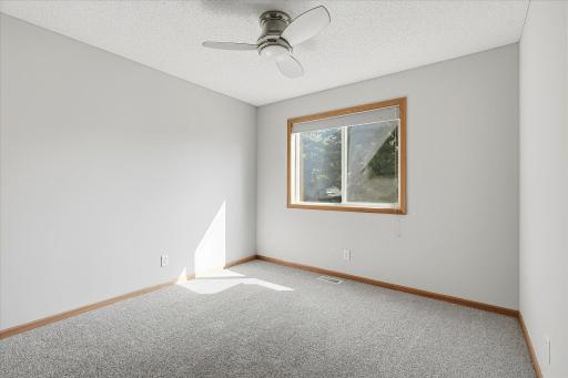 Bright upper-level bedroom features neutral décor, newer carpet, a ceiling fan, and a large window