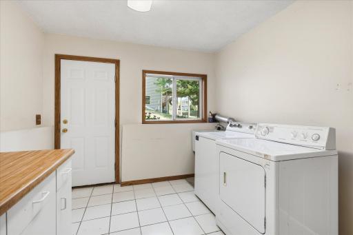 Spacious laundry room features a utility sink, cabinetry, countertop workspace, tile flooring, natural light, and convenient garage access.