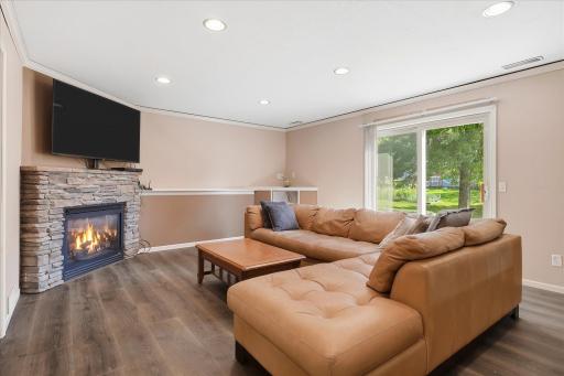 Spacious lower-level family room offers plenty of room for relaxing and entertaining, featuring LVP flooring, recessed lighting, crown molding, and a stone-surround gas fireplace.