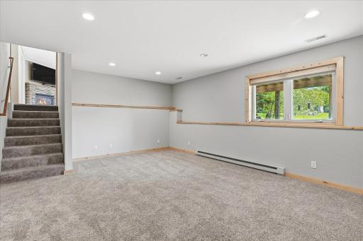 Spacious lower-level bonus room/bedroom features fresh neutral finishes, plush carpeting, recessed lighting, and a large window for natural light.