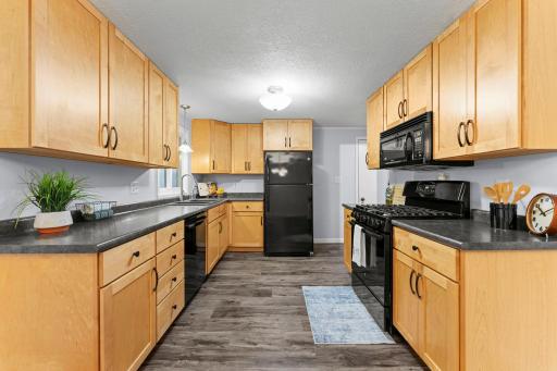 The kitchen offers luxury plank flooring that extends into the nearby dining room, along with ample wood cabinetry, generous countertop space, and sleek black appliances.