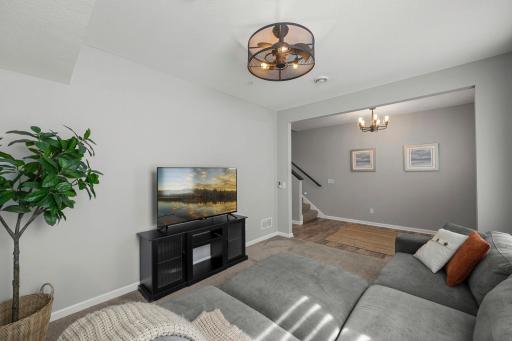 To the left, a spacious family room features carpeting, a unique ceiling fan and light fixture combination, and a large window that fills the space with natural light.