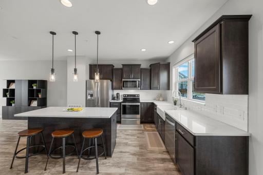 The kitchen features ample cabinetry, quartz countertops, a spacious center island with breakfast bar seating, pendant and recessed lighting, stainless steel appliances, and a walk-in pantry.