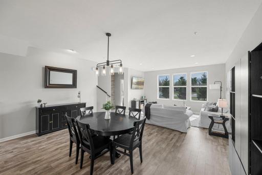 The kitchen flows seamlessly into the dining area, highlighted by a modern hanging light fixture, and into the bright living room with large windows that invite abundant natural light.