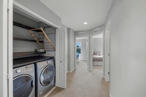 Rounding out the upper level is a centrally located laundry closet with a front-loading Whirlpool washer and dryer, shelving, and pull-down drying racks to make laundry day a breeze.