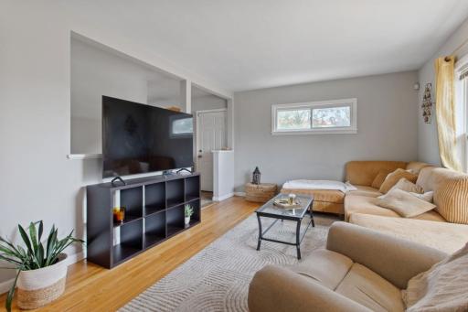 Light and bright living room with gleaming hardwood floors and fresh paint, featuring an eastern transom window and door leading to the fenced backyard and concrete patio. Also shown is the entrance to the finished basement.