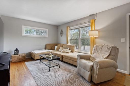 A second view of the bright, inviting living room showcases south-facing windows, a transom window bringing in additional eastern light, and beautiful gleaming hardwood floors that add warmth and character. Enjoy many morning coffees or movie nights