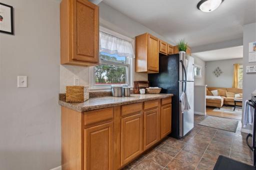 Bright, fresh kitchen featuring generous cabinetry and a spacious baking/cooking area. A beautiful window overlooks the side patio and barbecue area, bringing in natural light and creating an inviting space for cooking and entertaining.