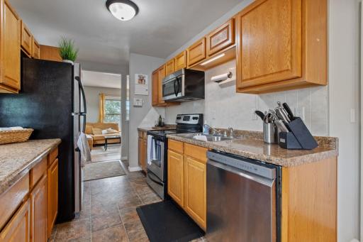 Another bright kitchen view highlights abundant counter space, stainless steel appliances, and natural light from the side window. The open view toward the living room and backyard door makes everyday living and entertaining easy.