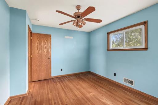 Cheerful main-level bedroom with hardwood floors, blue walls, two windows, and a ceiling fan.