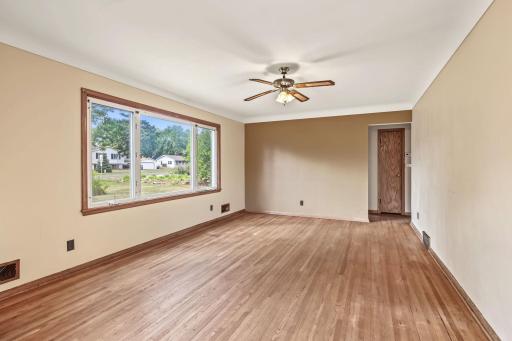 Bright living room featuring hardwood floors, a wide picture window, ceiling fan, and warm wood trim.