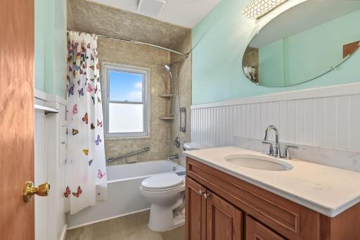 Main-level full bathroom featuring a long vanity, tub and shower, window, and convenient built-in storage.