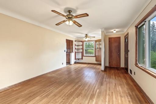 Spacious main-level living room featuring hardwood floors, large windows, two ceiling fans, and neutral finishes.