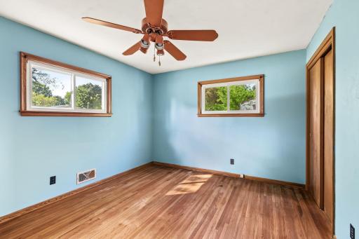 Main-level bedroom with hardwood floors, two windows, ceiling fan, and cheerful blue walls.