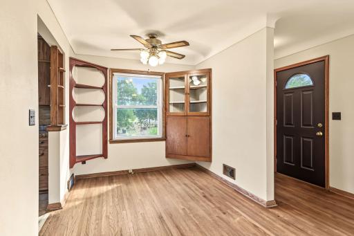 Light-filled dining area featuring hardwood floors, built-in display shelving, a ceiling fan, and welcoming front entry.