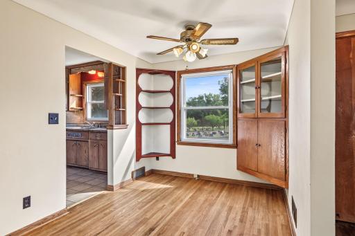 Dining area featuring hardwood floors, built-in glass-front cabinetry, ceiling fan, and convenient kitchen access.