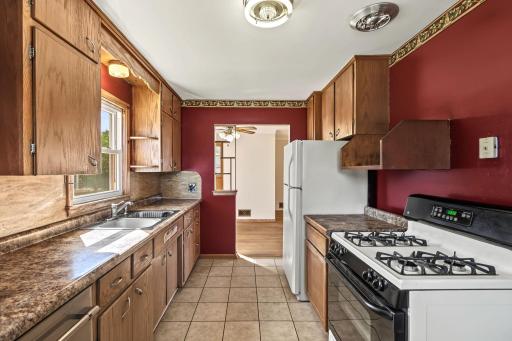 Galley kitchen offering generous cabinetry and counter space, gas range, durable tile flooring, and backyard access.