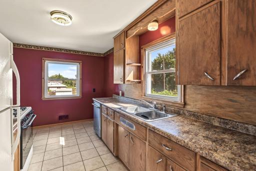 Galley kitchen featuring wood cabinetry, generous counter space, tile flooring, and a window above the sink.