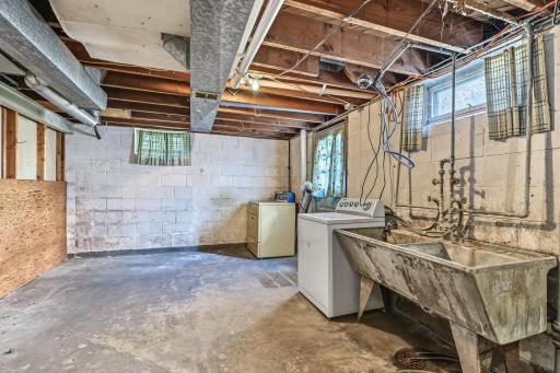 Unfinished laundry and utility area with a utility sink, mechanical access, concrete flooring, and additional storage space.