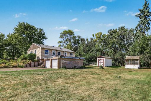 Wide backyard view showcasing the detached garage, storage shed, raised garden beds, and open lawn.