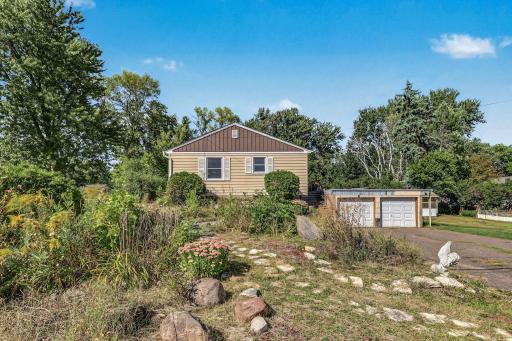Rear exterior view showcasing the home's spacious yard, established gardens, mature landscaping, and detached garage.