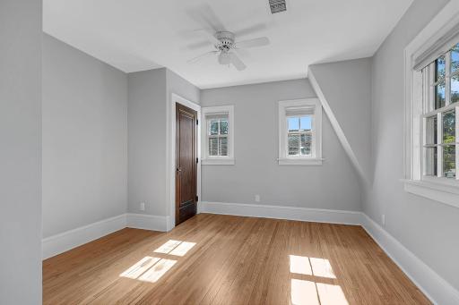 A bright second upper-level bedroom featuring multiple windows for abundant natural light and a ceiling fan for added comfort.