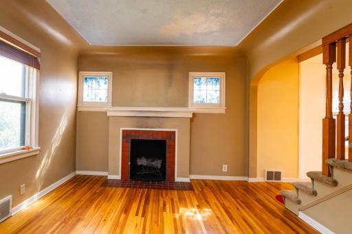 Two glass pane windows flank the wood burning fireplace. Large archway with access to staircase and dining area.
