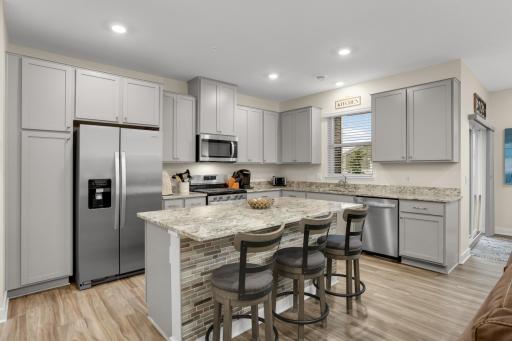 Spacious kitchen featuring a large center island, granite countertops, abundant counter space, and stainless-steel appliances. A bright kitchen window overlooks the covered patio, creating a welcoming connection to the outdoor living space.