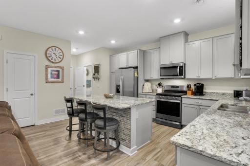 Spacious kitchen featuring a large center island, granite countertops, abundant counter space, and stainless-steel appliances. A bright kitchen window overlooks the covered patio, creating a welcoming connection to the outdoor living space.