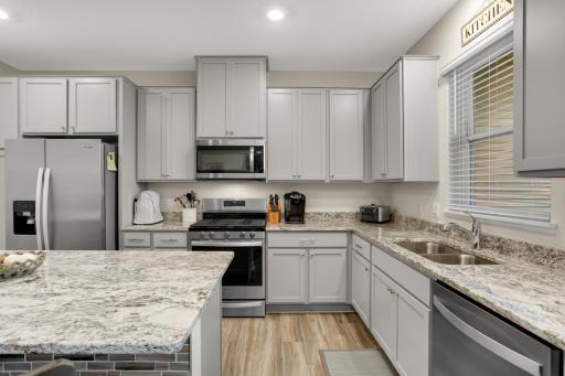 Spacious kitchen featuring a large center island, granite countertops, abundant counter space, and stainless-steel appliances. A bright kitchen window overlooks the covered patio, creating a welcoming connection to the outdoor living space.