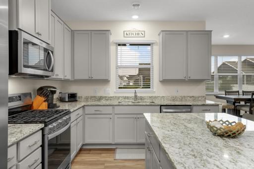 Spacious kitchen featuring a large center island, granite countertops, abundant counter space, and stainless-steel appliances. A bright kitchen window overlooks the covered patio, creating a welcoming connection to the outdoor living space.