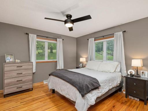Spacious main-level bedroom with hardwood floors, two windows, and a new ceiling fan.