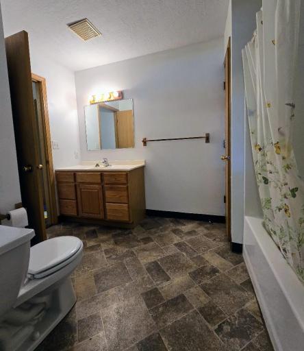 Full bath with vinyl flooring, tub with shower, stool, & linen closet.